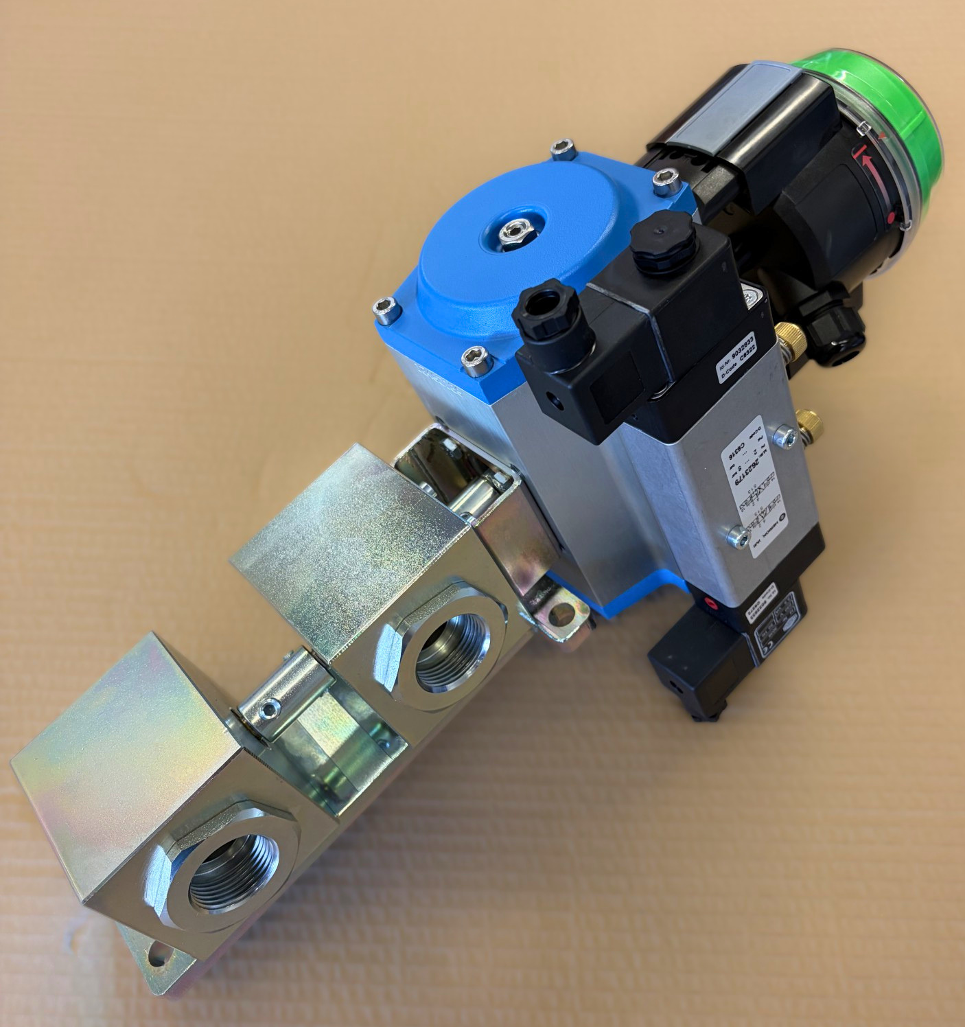 Folge 7_Schnappschuss der Woche - vonScheven Industrial solenoid valve with blue actuator and green status indicator on a metallic block, against a cardboard background.
